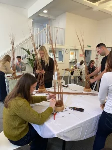 People stood and sat around a table using willow branches to make bird feeders