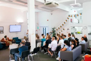 A group of people sat on chairs watching someone do a talk at the front of the room