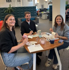 Three people sat round a table in an office painting mugs