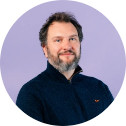 Portrait of a man wearing a black quarter zip jumper against a purple background